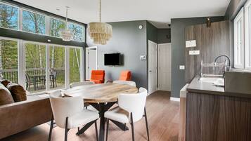 A modern kitchen with a wooden island, a dining area with a large table and chairs, and a TV mounted on the wall.