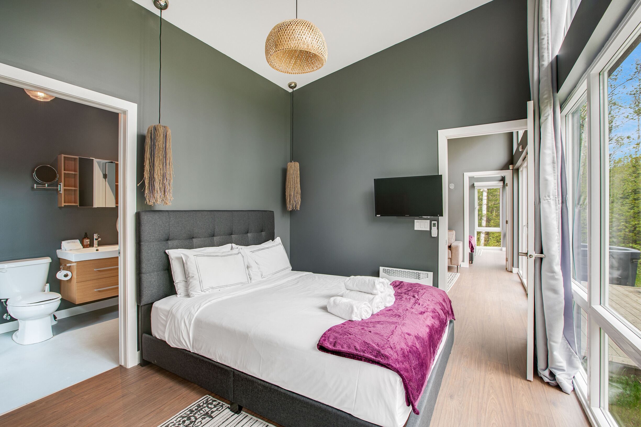 A modern bedroom with a large bed, a television, and a view of the outdoors.