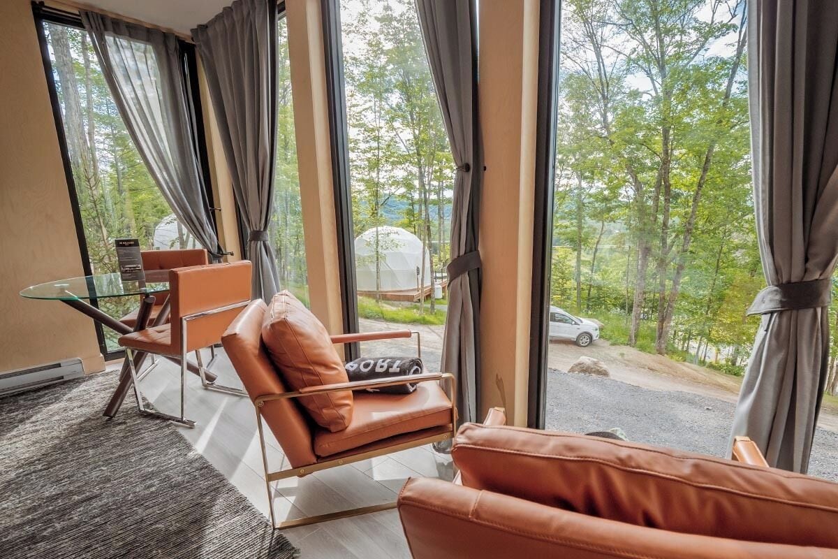 A room with large windows, a glass table, leather chairs, and a view of a road and trees.