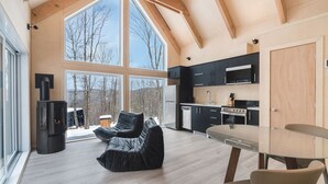 A modern interior with a large window, a black leather sofa, a dining table, and a kitchen area.