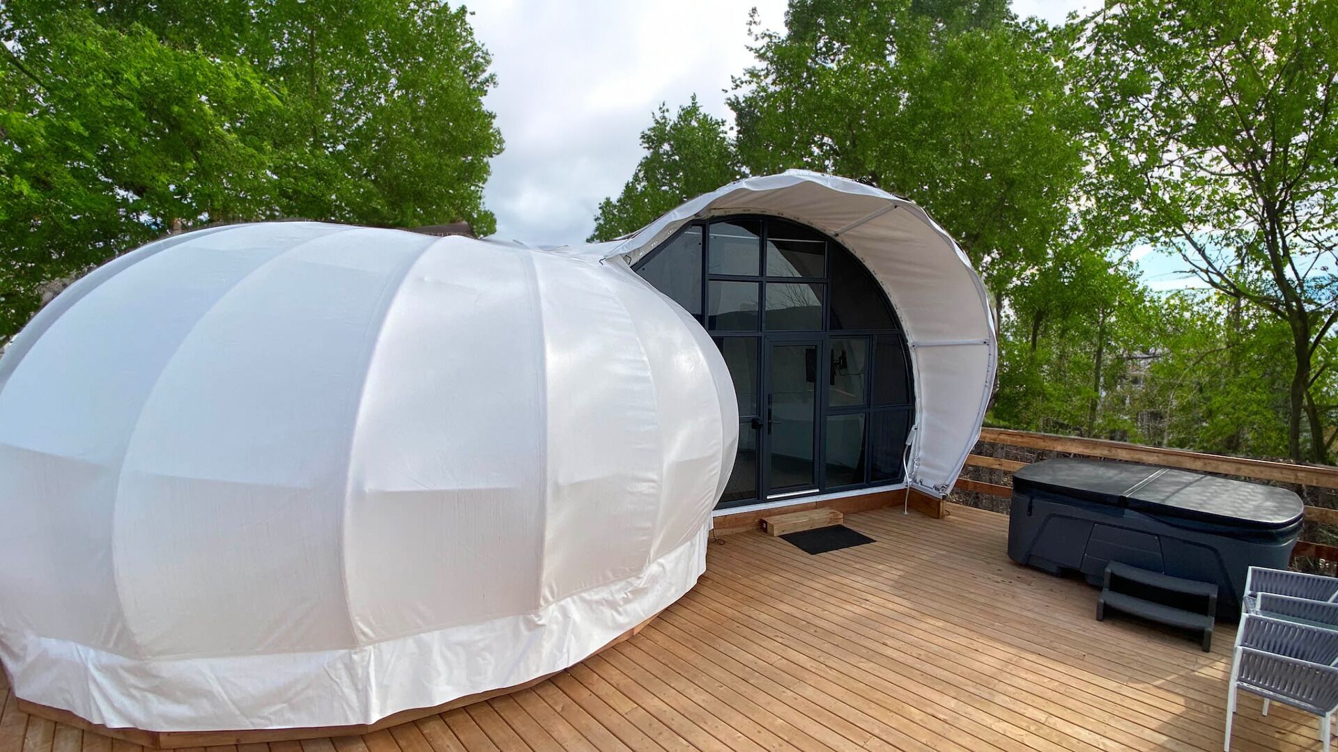 Una estructura en forma de cúpula con una puerta de cristal, una terraza de madera y un jacuzzi.