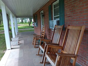 A covered porch with wooden rocking chairs, a brick building, and a car parked outside.