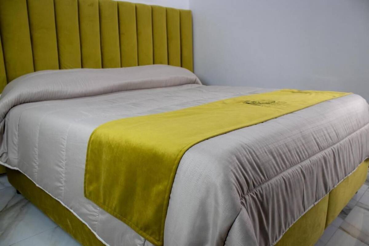Uma cama com cabeceira, um edredom cinza e amarelo, e um cobertor amarelo.