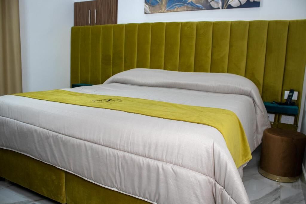 A hotel room with a bed, a headboard, a nightstand, and a brown cylindrical object.