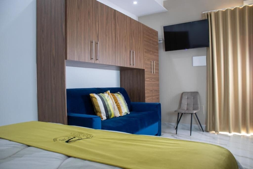 A hotel room with a bed, a blue sofa, a TV mounted on the wall, and a chair.