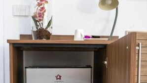 A wooden cabinet with a built-in mini-fridge, a vase with flowers, and a desk lamp. - Augustea Travel (San Marcellino)