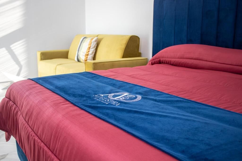 Un lit recouvert d’une couverture bleue et rouge, un fauteuil jaune et un rideau bleu.