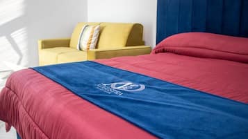 Un lit recouvert d’une couverture bleue et rouge, un fauteuil jaune et un rideau bleu.