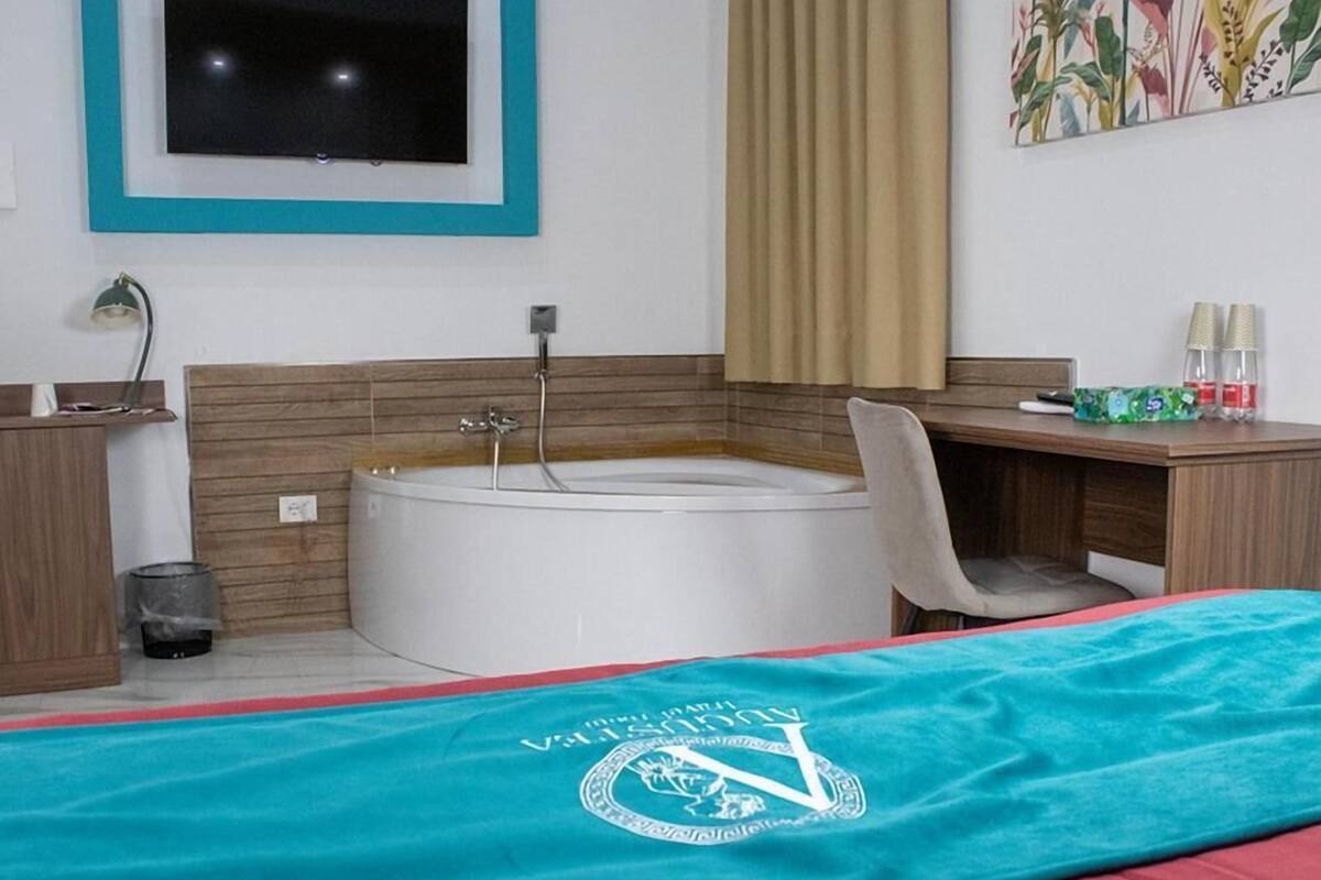 Quarto de hotel com cama, escrivaninha, cadeira, banheira e televisão.