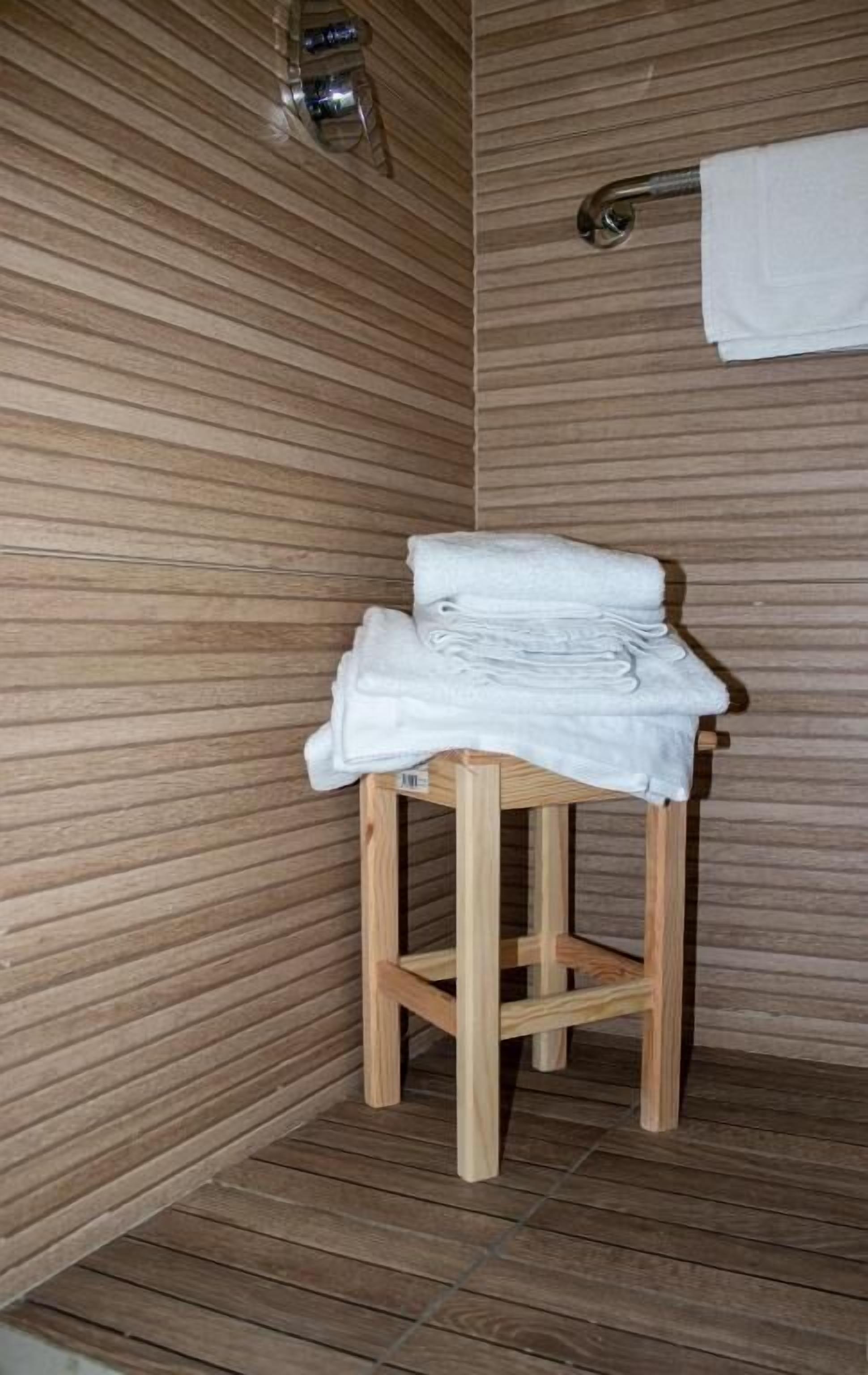 A wooden stool with a folded towel in a room with wooden panel walls and a wooden floor.