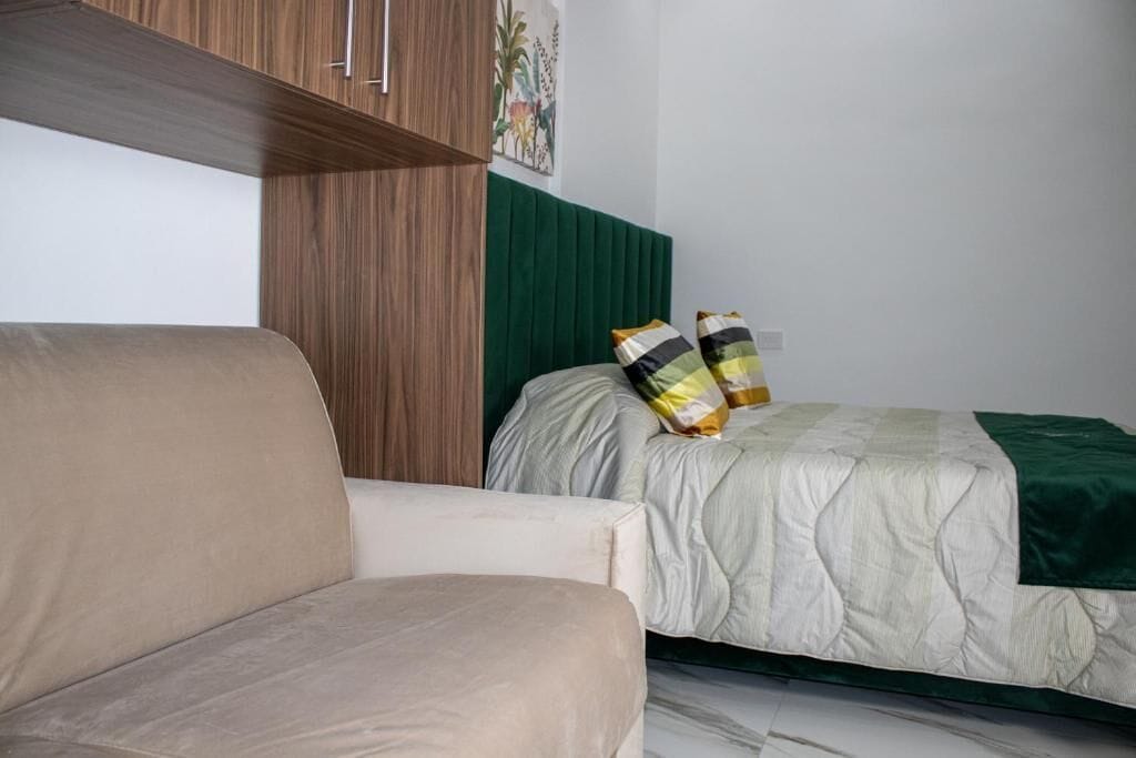 A bedroom with a bed, a green headboard, a beige sofa, and a wooden cabinet.