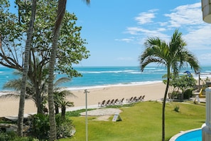 Vista sulla spiaggia con palme, piscina e poltrone da relax.