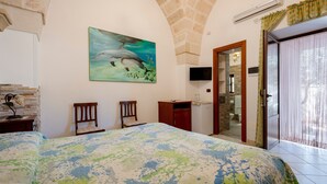A bedroom with a bed, a painting of dolphins, a TV, a desk, and a bathroom visible through an open door. - Villa Tonia - Stanza Edera Apartment with Private Terrace, Wi-Fi, and Air Conditioning (Fasano)