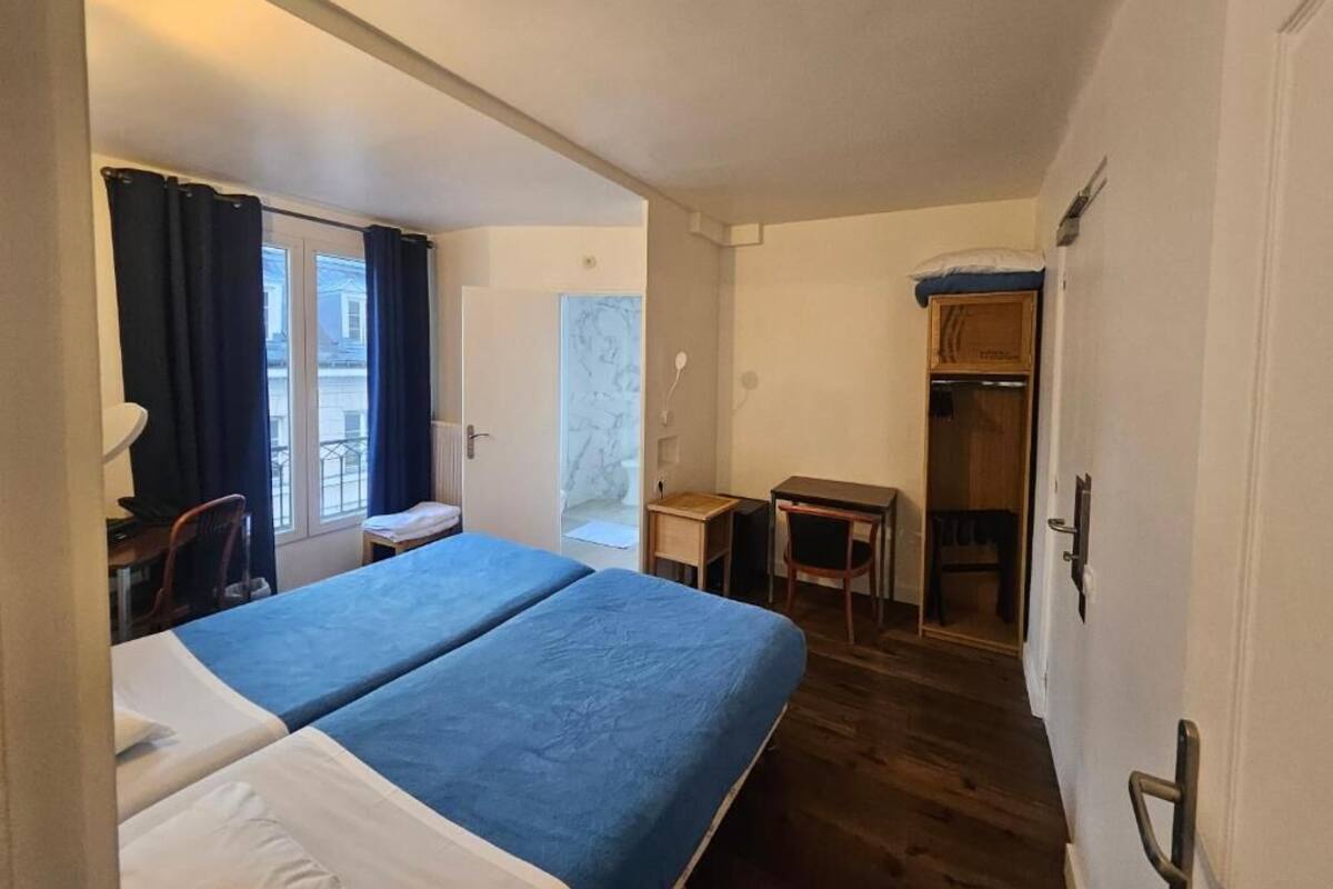 A room with two beds, a desk, a chair, a wardrobe, and a window with curtains.