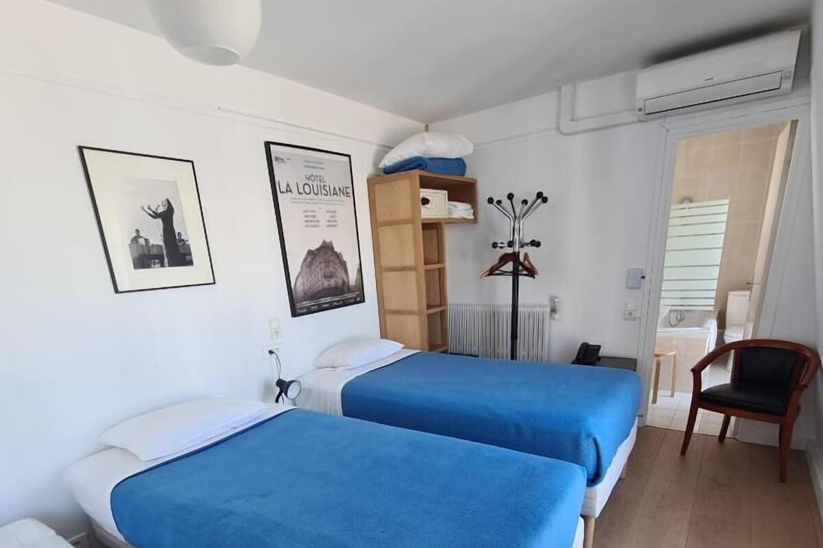 A hotel room with two beds, a wooden chair, a coat rack, and a poster on the wall.