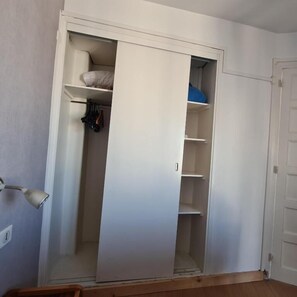 A white closet with shelves and hanging space, a wooden floor, and a closed door. - HOTEL LA LOUISIANE (Paris)