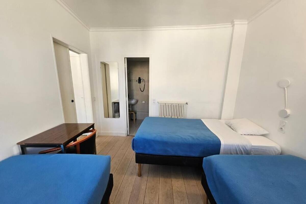 A room with two beds, a desk, a radiator, and a bathroom visible through an open door.