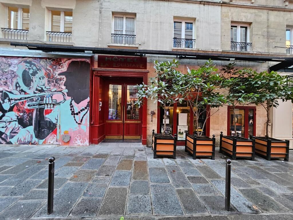 A hotel facade with a red entrance, a mural on the left, and outdoor seating.
