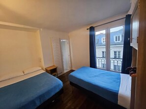 Una stanza con due letti, una finestra con tende, un termosifone e vista sui palazzi esterni.