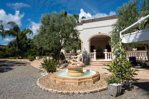 Ein Innenhof mit einem Brunnen, Palmen und einem Gebäude mit einem Bogen.