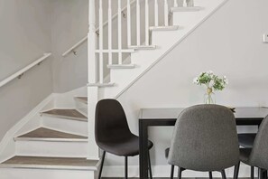 A staircase with white railings and wooden steps, a dining table with chairs, and a vase with flowers on the table. - Modern 4BD 2BA Home Near Downtown Metra (Highland Park)