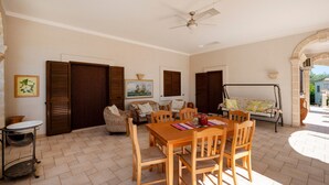 Un comedor con mesa y sillas de madera, ventilador de techo y vista al exterior.