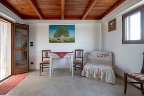Ein Zimmer mit Holzboden, einem Baumgemälde, einem weißen Sofa mit der Stickerei 'LOVE', einem Tisch mit Stühlen und einer Tür mit Glasfenster.