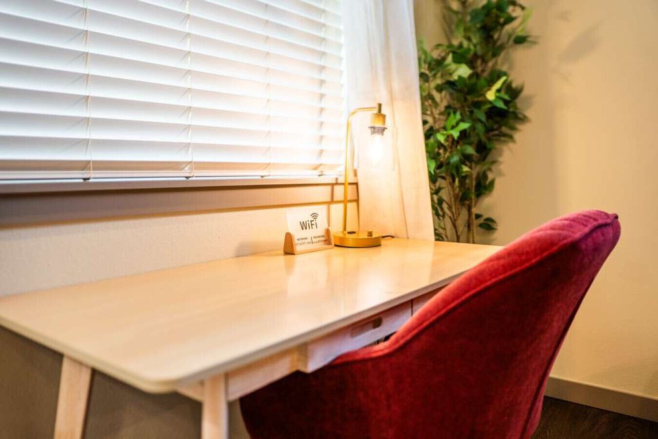 Een kamer met een houten bureau, een rode stoel, een lamp en een plant.