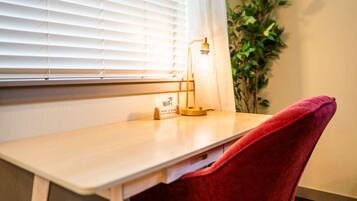 Een kamer met een houten bureau, een rode stoel, een lamp en een plant.