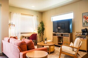 Un salon comprenant un canapé, des fauteuils, une table basse, un téléviseur et une bibliothèque.