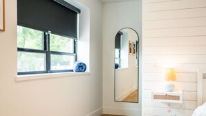 Ein Badezimmer mit Fenster, Spiegel, Lampe und einem Wandregal.