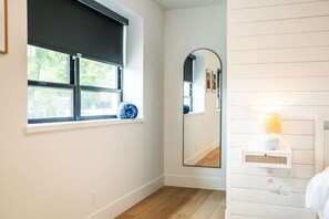 Ein Badezimmer mit Fenster, Spiegel, Lampe und einem Wandregal.