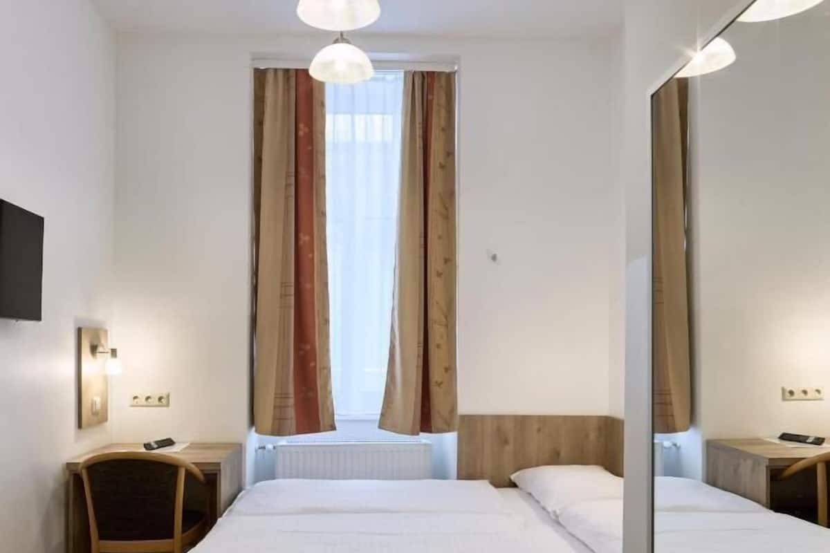 Habitación de hotel con dos camas, piso de madera, un ventanal con cortinas, televisor de pantalla plana y un espejo.