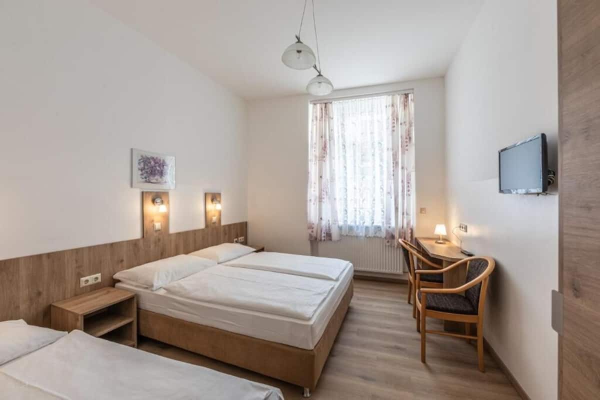 Habitación de hotel con dos camas, un escritorio con silla, televisor y ventana con cortinas.
