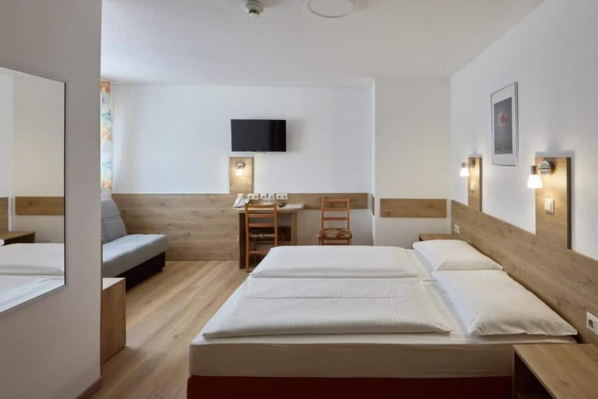 Habitación de hotel con dos camas, un escritorio, una silla, un televisor y luces fijadas a la pared.