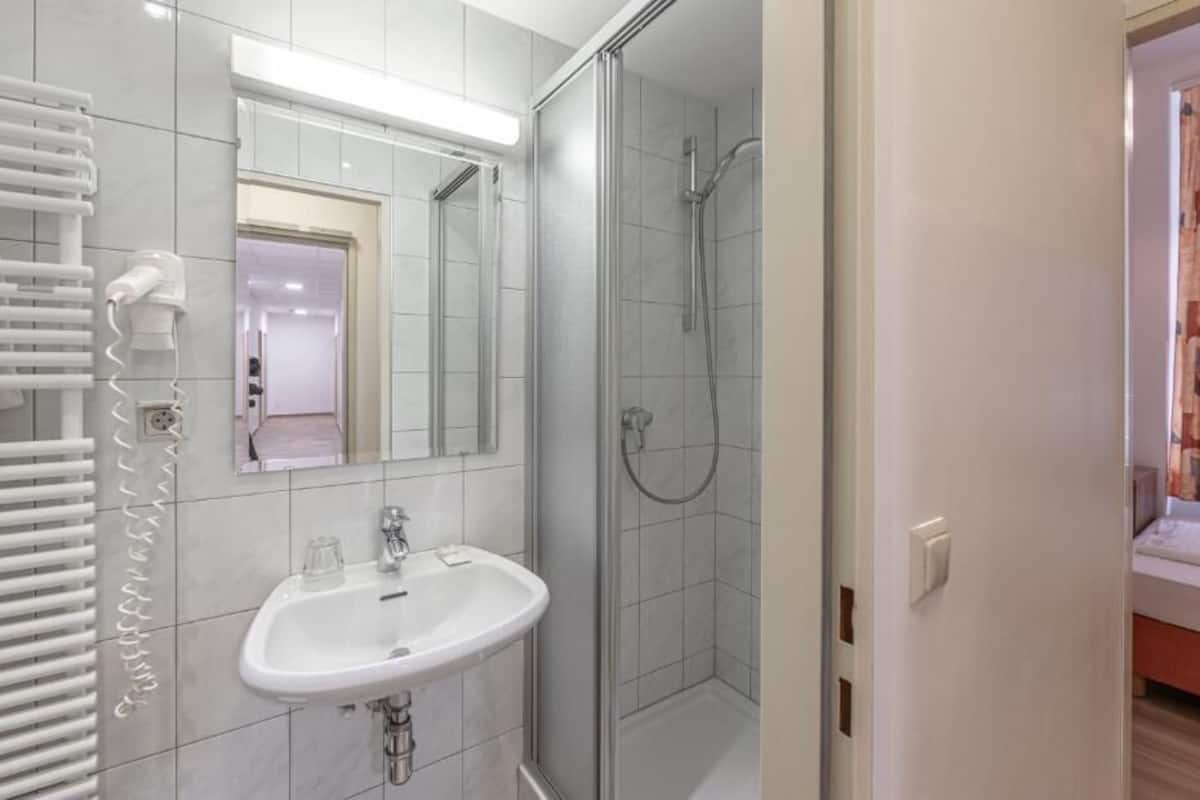 Un baño con un lavabo blanco, un espejo, cabina de ducha de vidrio y un perchero para toallas.