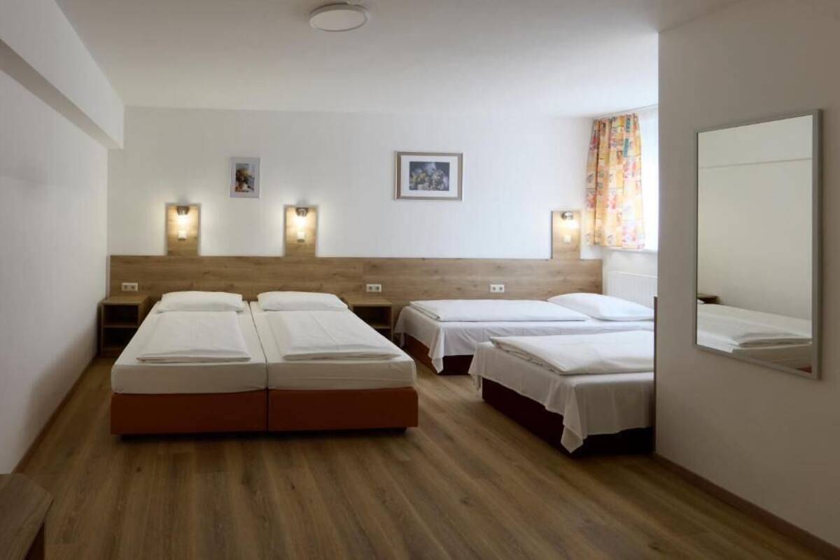 Habitación de hotel con dos camas, suelo de madera, cabecero, luces fijadas a la pared y un espejo.