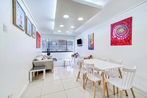 Un salon moderne comprenant un canapé, une table à manger et des chaises, un téléviseur fixé au mur et des œuvres d’art accrochées aux murs.