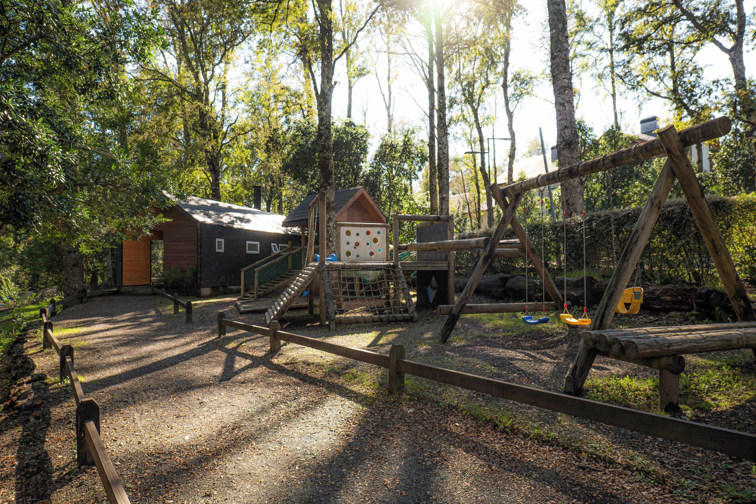 Une aire de jeux avec des structures en bois, un petit bâtiment et un espace abrité.
