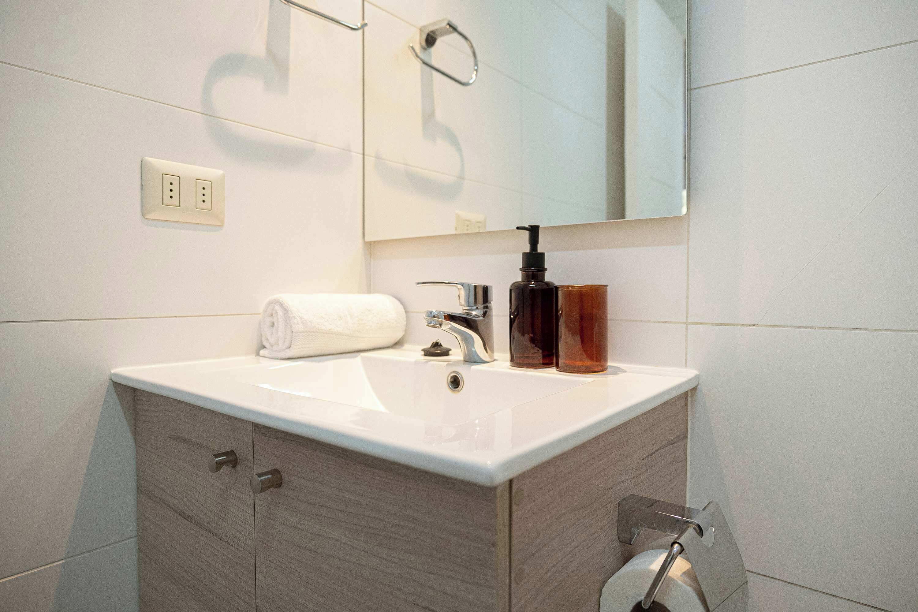 A bathroom with a white sink, a mirror, a towel, and a soap dispenser.