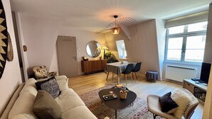 A living room with a sofa, a coffee table, a dining table with chairs, a mirror, and a television. - Quiet 2-bdrm flat in central Strasbourg (Strasbourg)