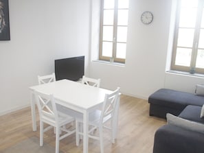 A room with a white table and chairs, a television, a sofa, and a clock on the wall. - Apartment with view on city of Carcassonne (Carcassonne)