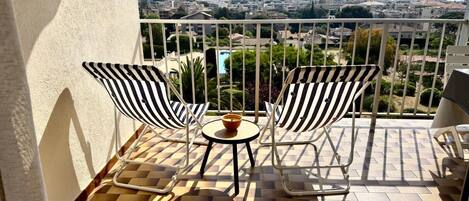 A balcony with two striped chairs, a small round table, and a bowl.