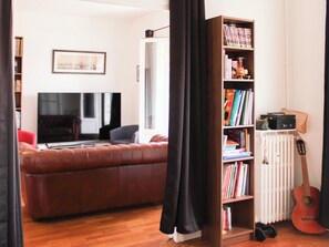 A living room with a brown leather sofa, a bookshelf, a guitar, and a radiator. - Bright balcony near Roland-Garros (Paris)