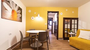 Una habitación con una mesa de comedor, sillas, un sofá, una lámpara y una puerta que da a otra habitación.