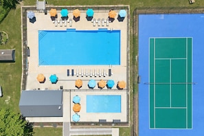 An aerial view of a pool area with a tennis court, multiple umbrellas, and lounge chairs.