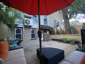 Eine Holzterrasse mit Gartenmöbeln, einem roten Sonnenschirm und Blick auf ein Wohngebäude.