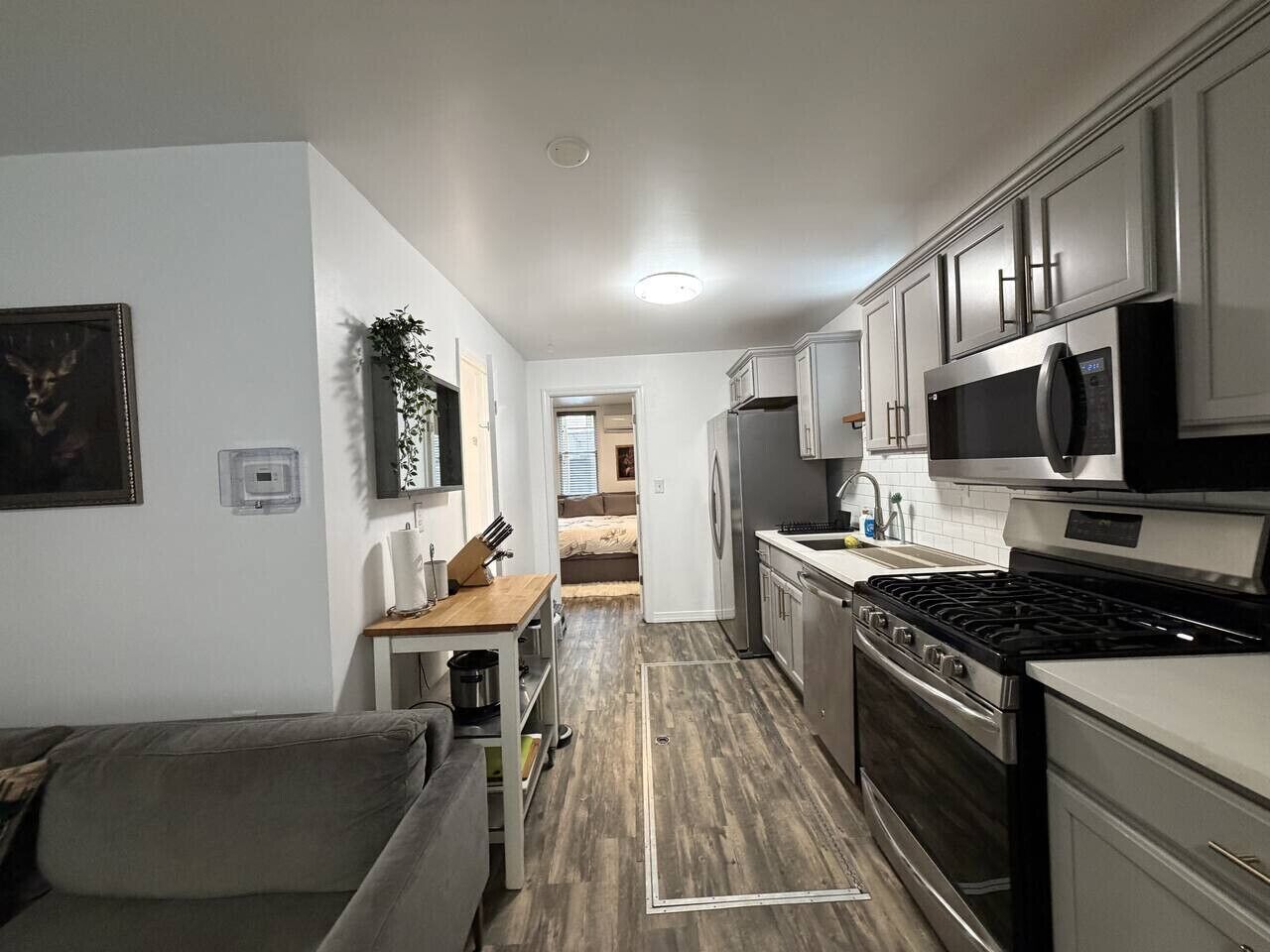 A compact kitchen with a stove, microwave, and refrigerator. A dining table and a couch are visible in the adjacent living area.
