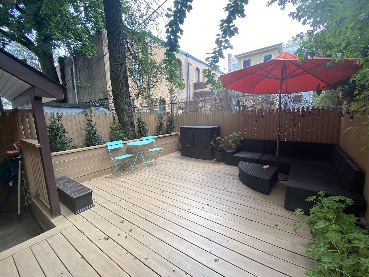 A wooden deck with outdoor furniture, a red umbrella, and a fence.