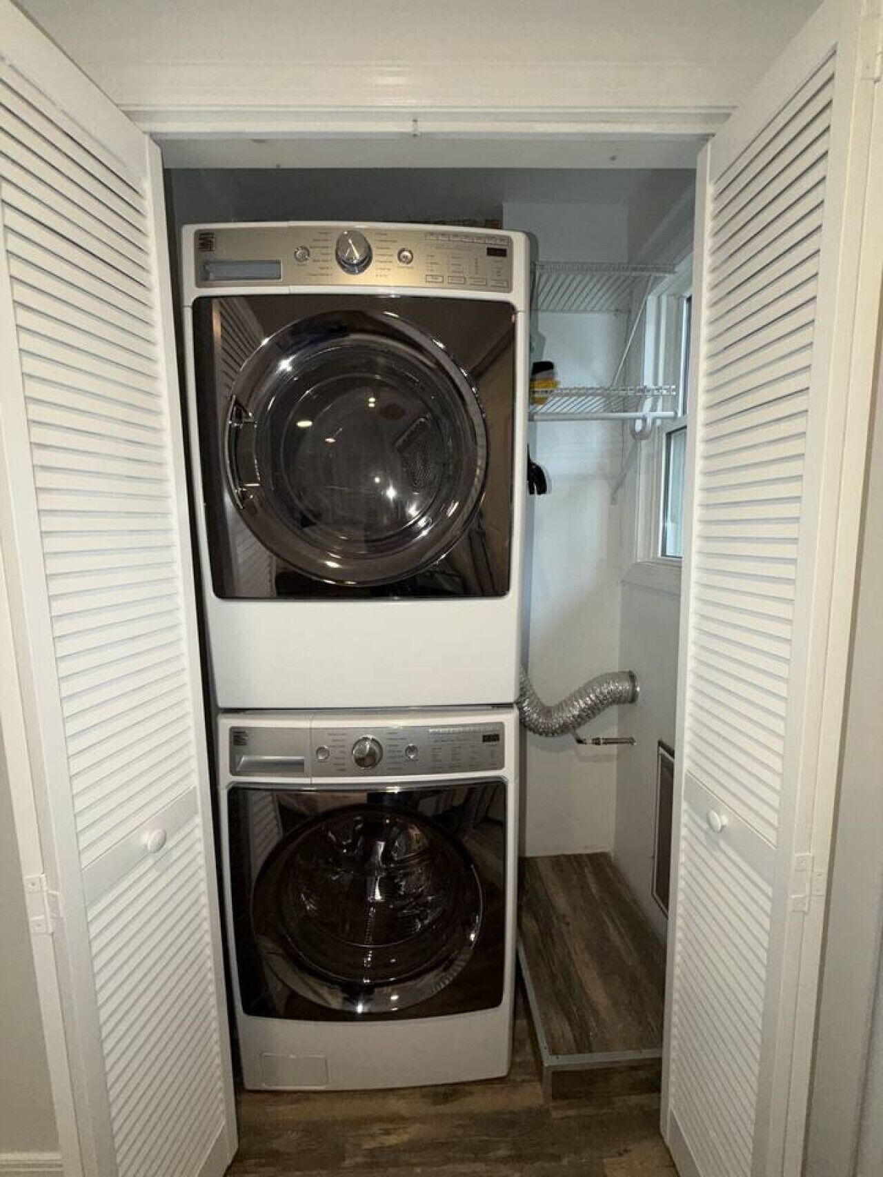 A laundry room with two stacked washers and dryers, a metal vent, and a wooden floor.